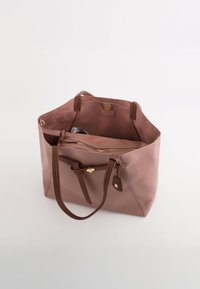 Różowa skórzana torba tote z brązowymi akcentami i uchwytami. Wnętrze ma gładką teksturę z zamykaną na zamek przegrodą i dodatkowymi kieszeniami.