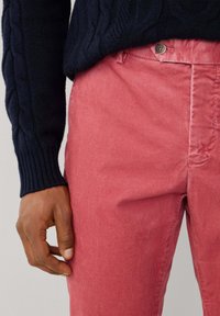 Rode corduroy broek met verticale ribbels, gecombineerd met een marineblauw gebreid sweater. Close-upweergave toont de gestructureerde stof en het knoopdetail.