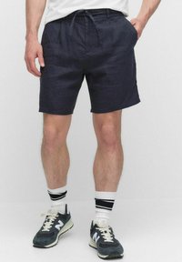 Marineblå linshorts med dragsko i midjan, med sidfickor. Matchas med grå sneakers och vita strumpor med svarta ränder.