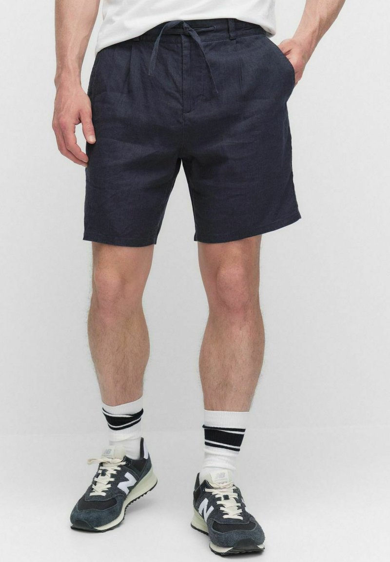 Marineblå linshorts med dragsko i midjan, med sidfickor. Matchas med grå sneakers och vita strumpor med svarta ränder.