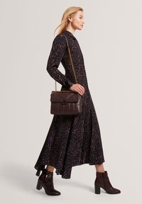 Abito nero a maniche lunghe con motivo floreale rosa, gonna fluente, abbinato a una borsa in pelle marrone scuro e stivaletti con tacco.