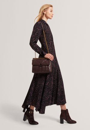 Zwarte jurk met lange mouwen en een roze bloemenpatroon, een vloeiende rok, gecombineerd met een donkerbruine lederen handtas en enkellaarsjes met hakken.