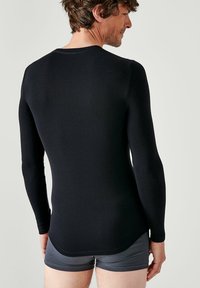 Zwarte lange mouwen top gemaakt van een gladde, rekbare stof, met een ronde hals en een licht gebogen zoom, gecombineerd met grijze shorts.