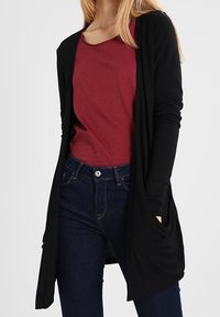 Czarny długi kardigan z otwartym przodem, lekki materiał, luźny krój, noszony na bordo t-shircie, w zestawieniu z ciemnymi dżinsami, styl casual.