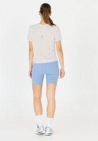 Ljust grå kortärmad topp med sprund bak, ihopparad med ljusblåanpassade shorts. Modellen bär vita strumpor och silverfärgade sportskor.