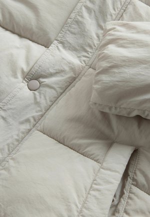 Vadderad jacka i ljusbeige med en texturerad yta, synliga sömmar, framträdande knapprubrik och en mjuk, stoppad krage.