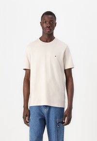 T-shirt beige à manches courtes en coton avec un col rond, arborant un petit logo sur la poitrine et une coupe décontractée.