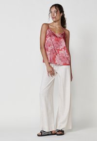 Haut sans manches à motifs floraux rouges avec finition en dentelle, associé à un pantalon large beige clair et des sandales noires avec des accents tissés.