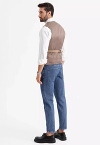 Braune Weste mit einem Rückenband, weißes Hemd, blaue Jeans und schwarze Schuhe, zeigt einen lässigen Look aus seitlicher und Rückansicht.