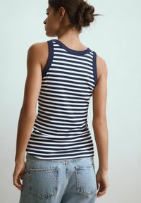 Navy og hvid stribet tanktop med tætsiddende design, brede stropper og rund halsudskæring, parret med lyseblå denim jeans.