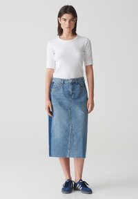 Jeansrock mit hohem Bund, ausgestattet mit einem Schlitz vorne und einem zweifarbigen Design. Kombiniert mit einem schlichten weißen Oberteil und blauen Sneakers.