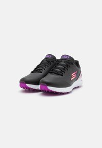 Czarne buty golfowe o smukłym designie, z purpurowym akcentem na podeszwie i logo, teksturowanym wierzchem oraz sznurowanym przodem.