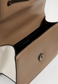 Bolso de cuero sintético marrón claro con un interior crema, que cuenta con un cierre de imán y un detalle de costura minimalista. El acceso abierto revela un compartimento espacioso.