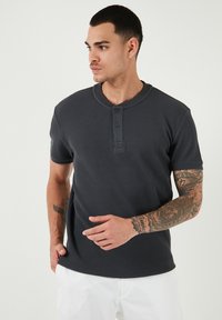 Maglietta henley grigia scuro a maniche corte con placket a tre bottoni e scollatura rotonda. Tessuto liscio, design aderente e spacco laterale.