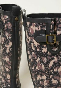 Rubber rain boots in black with a pink and beige abstract pattern. Features a black top trim and side buckle detail for adjustment.