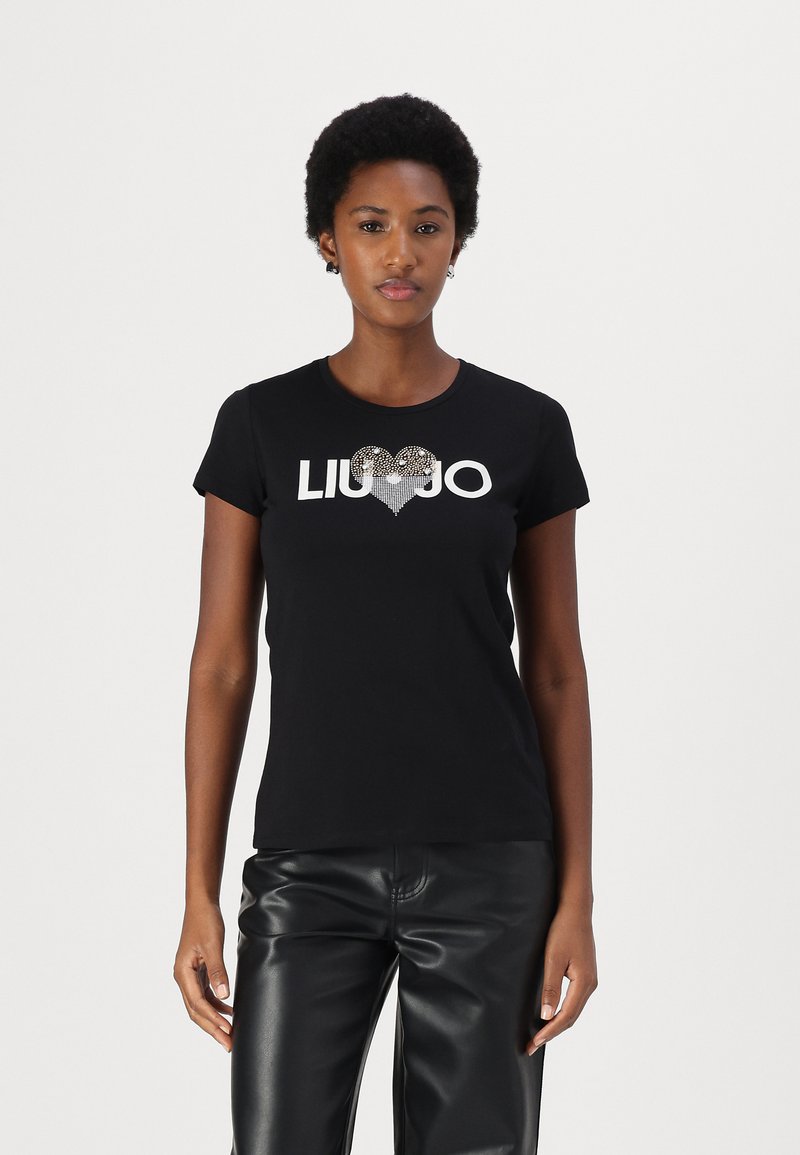 Mustat t-paidat, joissa on lyhyet hihat, ja joissa on hopeinen "LIU JO" -logo ja sydämen muotoilu, jotka on koristeltu strasseilla. Yhdistetty mustiin nahkahousuihin.