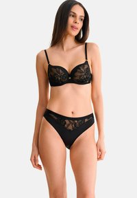 Ensemble de lingerie noire comprenant un soutien-gorge balconnet avec superposition en dentelle et accessoires dorés, associé à une culotte taille haute assortie avec des accents en mesh.