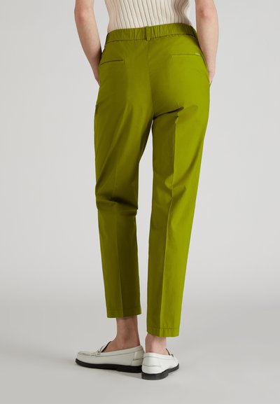 Pantalones verdes hasta el tobillo con una textura suave, cintura elástica y dos bolsillos traseros, combinados con mocasines blancos.
