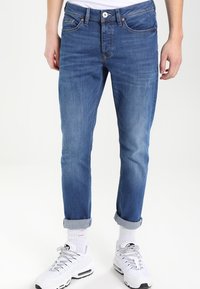 Slim-fit blå denimjeans med lätt blekning, fem fickor och uppvikta fållar, tillsammans med vita sportiga sneakers.