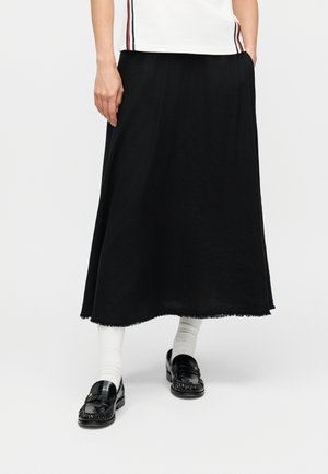 Osoba ubrana w czarną spódnicę midi, białe skarpetki, czarne mokasyny i biały top z czerwonymi i czarnymi paskami po bokach.