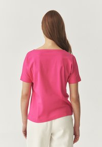 Top de manga corta, de color rosa brillante, con un ajuste relajado y un amplio escote estilo barco, hecho de una tela suave. La parte posterior es sencilla, sin adornos.