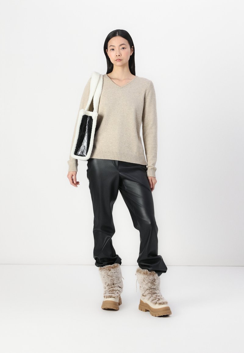 Sweater beige à col en V, pantalon en simili cuir noir et bottes beige moelleuses. Sac avec un extérieur pelucheux blanc et un intérieur noir.