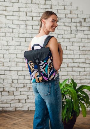 Rucksack mit schwarzem Klappdeckel und lebendigem Blumenmuster in Lila, Blau und Beige, hergestellt aus strapazierfähigem Stoff. Verstellbare Schultergurte.