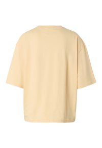 Μπλούζα oversized κρεμ με κοντά μανίκια και στρογγυλή λαιμόκοψη, εμφανιζόμενη από πίσω σε λευκό φόντο.