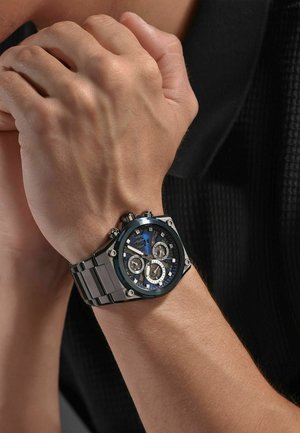 Chronograph-Uhr mit blauem Zifferblatt, silberfarbenen Akzenten und einem schwarzen Metallarmband. Verfügt über ein strukturiertes Gehäuse und mehrere Sub-Zifferblätter.
