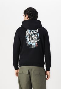 Felpa nera con cappuccio caratterizzata da un design grafico con il testo "SANTA CRUZ" e un'illustrazione di uno squalo. Tessuto morbido con una vestibilità comoda.