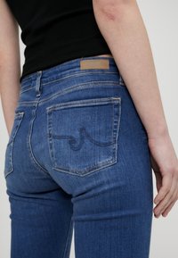 Höga blå denimjeans med slim fit, som har två bakfickor och en brun etikett vid midjan. Texturerat material med sömnadsdetaljer.