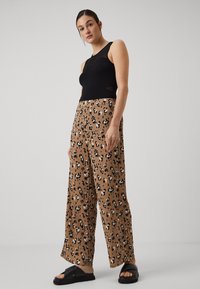 Sorte ermeless topp med mesh-detaljer, paret med brune bukser med vide ben og svart-hvitt leopardmønster, fullført med svarte sandaler.