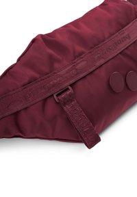 Burgunderfarbener Nylonbeutel mit einer weichen, gepolsterten Oberfläche, der zwei runde Knöpfe und einen gemusterten Gurt für einen sicheren Verschluss hat.