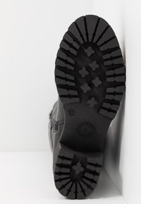 Suela de bota de goma negra con patrones de relieve profundos, que presenta tacos en forma de x para mayor tracción. Marcada con la talla 37 y un sello de logo.