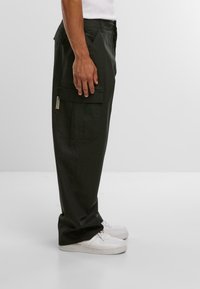Schwarze Cargo-Hosen in lockerer Passform, mit seitlichen Taschen und einem kleinen Markenlabel. Kombiniert mit weißen Sneakers.