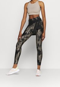Svarta leggings med ett brunt djurmönster, matchade med en beige kort topp och ett svart knytet midjeskärp. Vita sneakers med gula detaljer.
