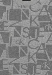 Tessuto grigio con un motivo ripetuto di grandi lettere nere sovrapposte e loghi "ck" in varie orientazioni.