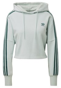 Zkrácená světle zelená mikina s kapucí vyrobená z měkké tkaniny má přední kapsu, šňůrku na kapuci a tmavě zelené boční pruhy s logem Adidas.