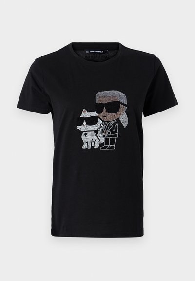 T-shirt en coton noir avec un graphique en strass d'une personne et d'un chat blanc, tous deux portant des lunettes de soleil. Encolure ronde et manches courtes.