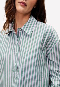 Hellgrünes und lilafarbenes gestreiftes Hemd mit Kragen, Knopfleiste und Brusttasche. Aus einem glatten Stoff mit lockerer Passform gefertigt.