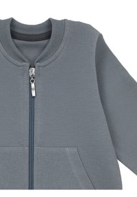 Szara bluza zapinana na zamek z prążkowanym kołnierzem, kieszeniami z przodu i kontrastowym zamkiem. Wykonana z miękkiej, fakturowanej tkaniny.