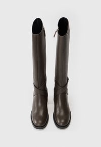 Un paio di stivali alti in pelle marrone scuro con punte rotonde, suole nere, cerniere laterali e fasce incrociate decorative alle caviglie su uno sfondo bianco.