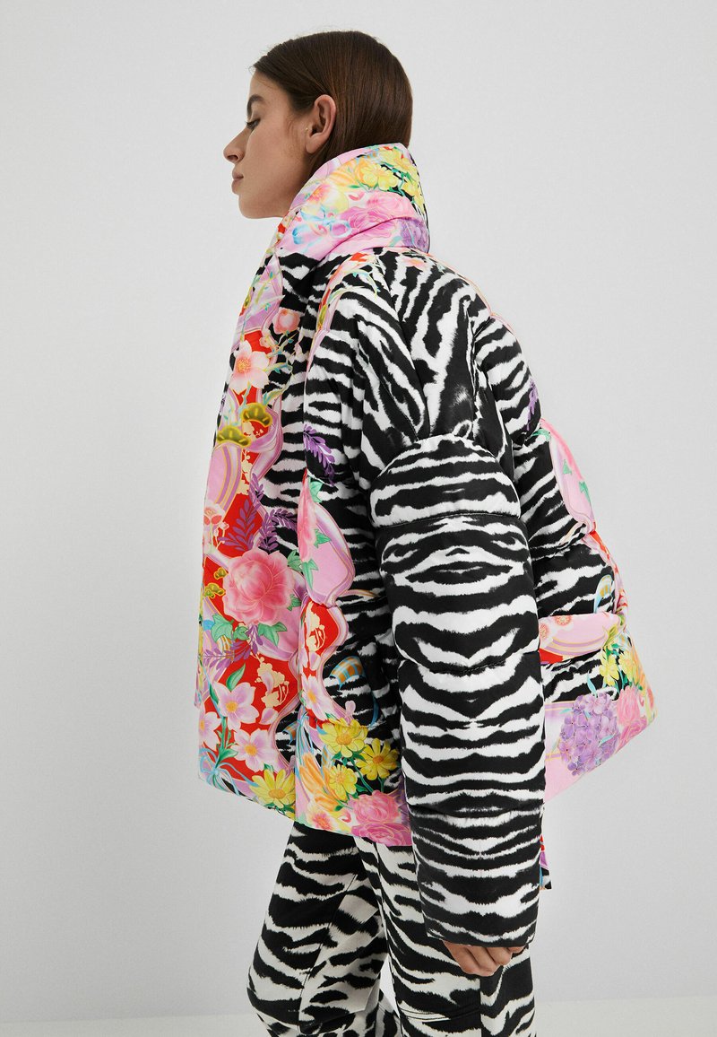 Kurtka puchowa z czarno-białym wzorem zebry, z kolorowym kwiatowym wzorem na kołnierzu i zdobieniach. Stylistyka dopasowana do spodni w tym samym stylu.