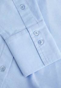Lichtblauw katoenen overhemdmanchet met drie knopen en zichtbare stiksels op de mouw.