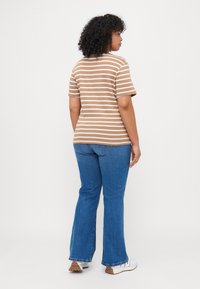 Camiseta a rayas marrón y crema, de manga corta, con corte holgado, combinada con vaqueros acampanados azules, y llevada con zapatillas blancas y suelas marrones.