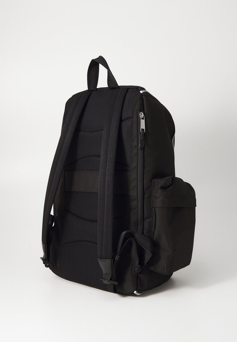 Sac à dos noir avec dos rembourré et bretelles réglables. Comprend une poche latérale et des fermetures éclair. Fabriqué en tissu durable.