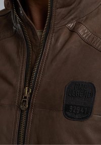 Giacca in pelle marrone con una finitura testurizzata, caratterizzata da una cerniera dorata e un'etichetta in tessuto nero con la scritta "PME LEGEND AMERICAN CLASSIC."