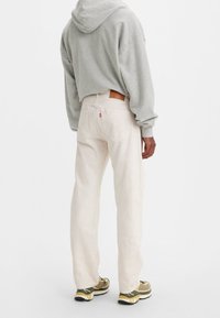 Vaqueros de mezclilla de color beige claro con corte recto, acompañados de una sudadera con capucha gris. Parche de cuero de marca notable en la parte trasera.
