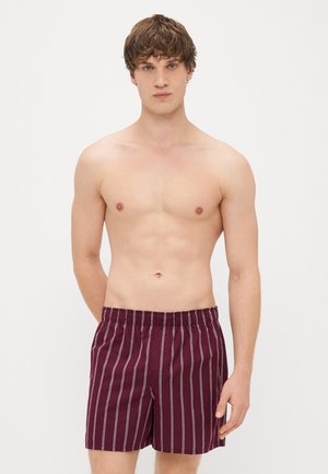 Calções de banho burgundy com riscas verticais brancas, apresentando uma cinta elástica. Tecido suave com um corte descontraído. Sem bolsos visíveis.