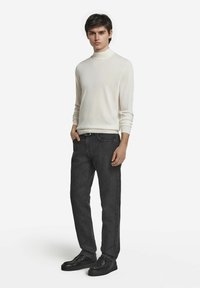 Vit mock-turtlenecktröja, grå jeans med slim fit, i kombination med svarta skor. Outfiten har minimala detaljer och en ren design.